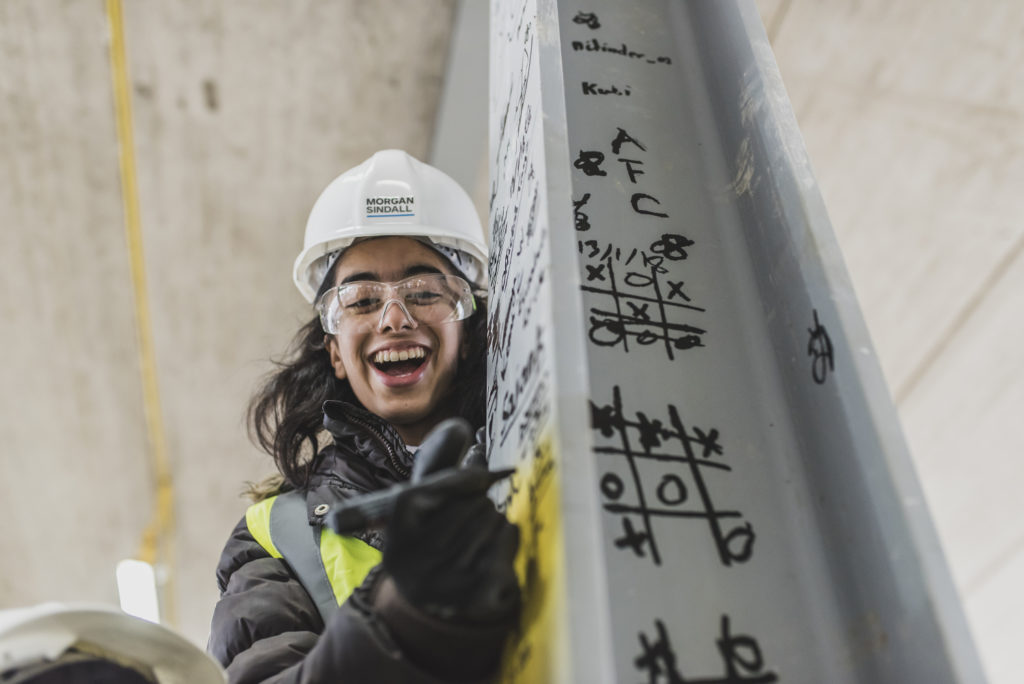 lady in a hard hat drawing on a concrete pillar