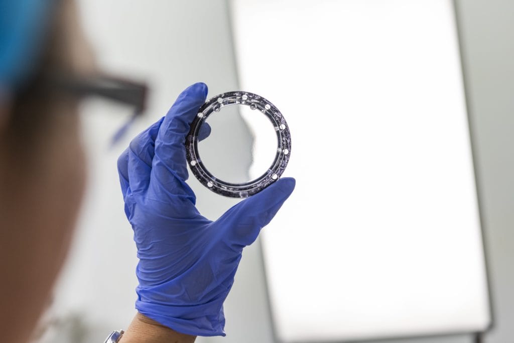 A hand in a blue latex glove inspects a metal disc