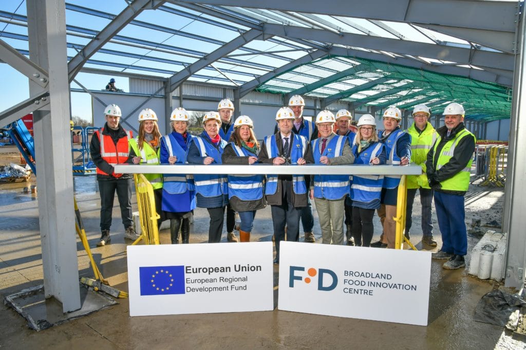 people in high vis jackets and hard hats sign the final steel on a building site